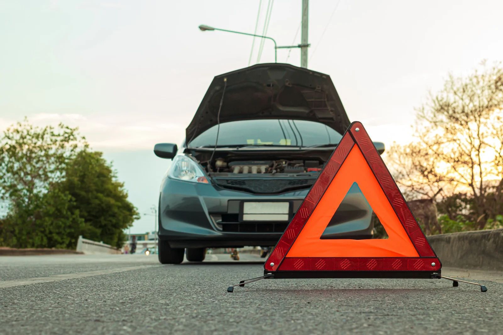 Car breakdown on roadside with warning triangle in front of a hatchback, hood open.