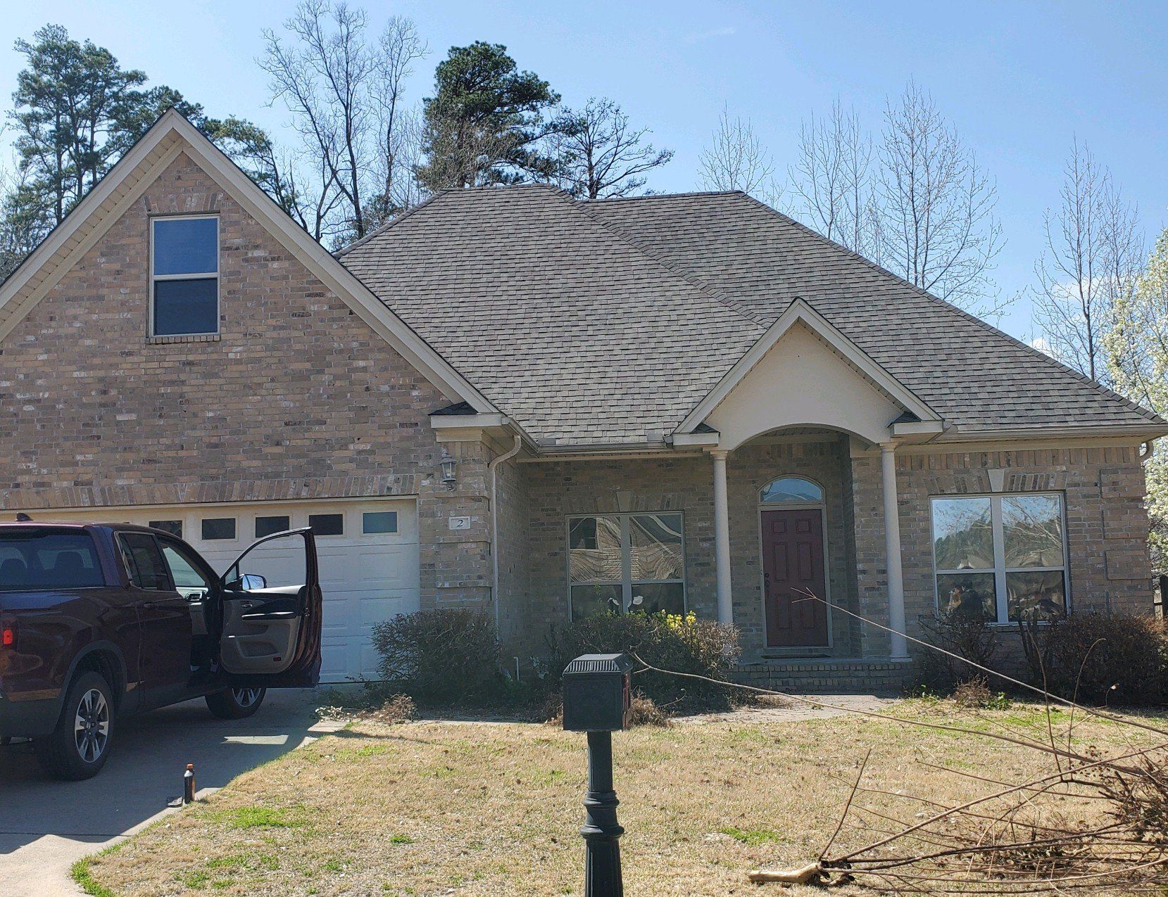 Brick suburban house with arched entry, dark roof, and a black SUV in the driveway under a clear sky