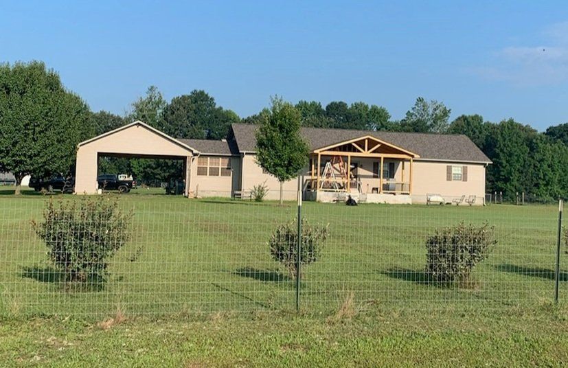A house is sitting in the middle of a grassy field behind a fence.