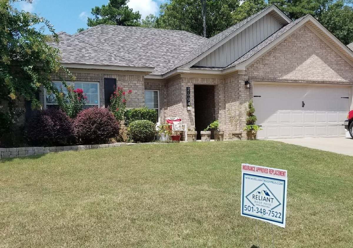 Suburban brick house with a for-sale sign on the lawn and a two-car garage