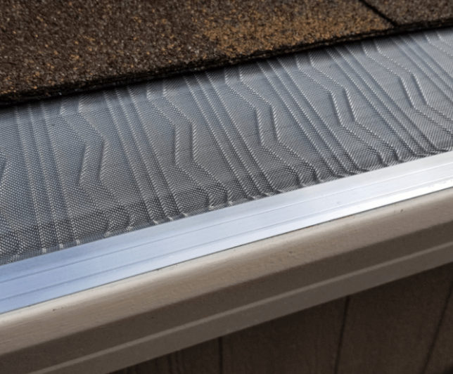 A close up of a gutter with a roof in the background.