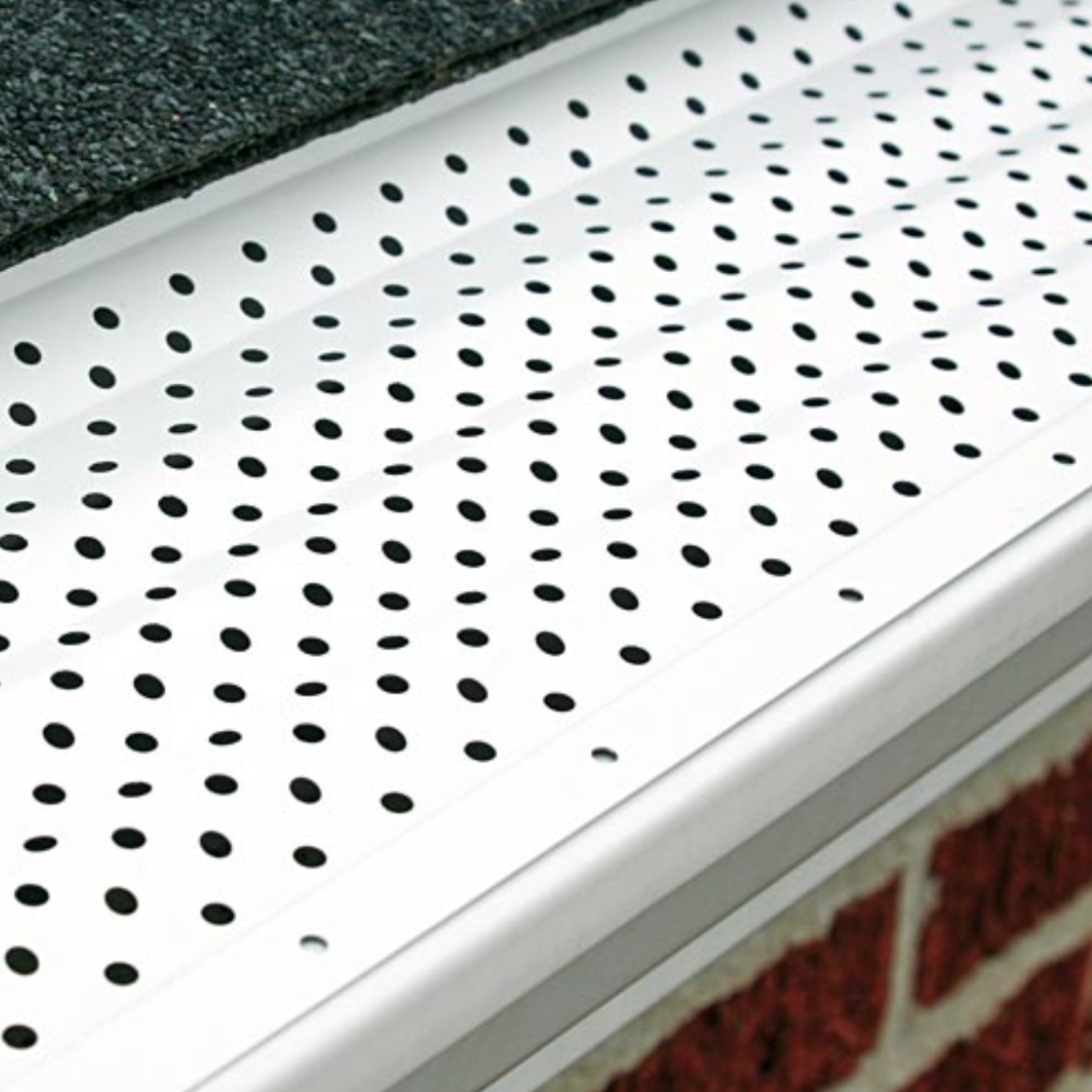 White perforated metal gutter guard along a roof edge above a brick wall