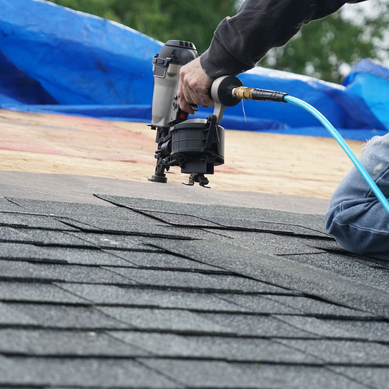 Damaged shingle roof with several torn sections exposing underlayment at sunset