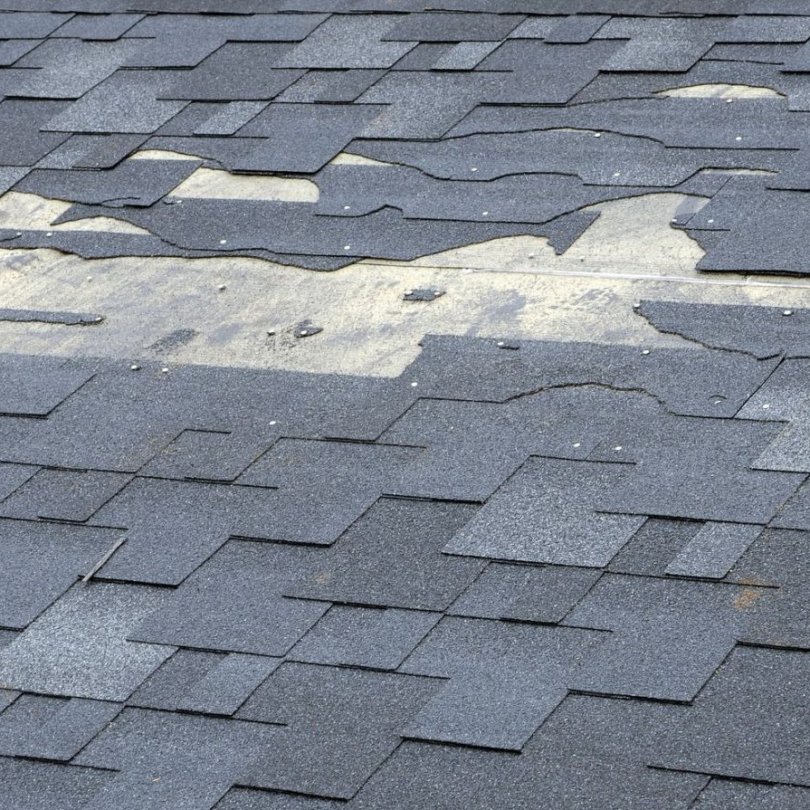 Damaged shingle roof with several torn sections exposing underlayment at sunset