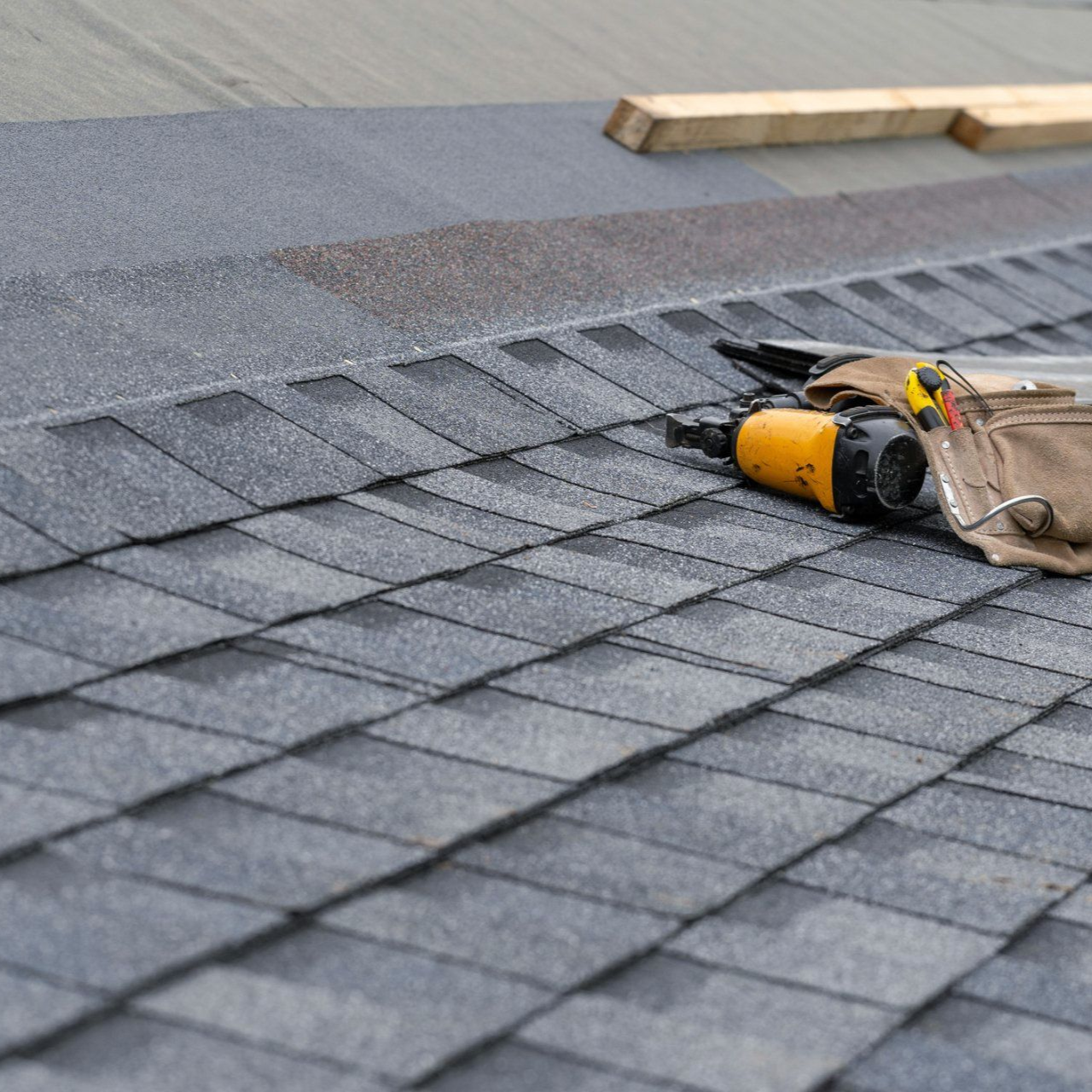Roof shingles with a yellow nail gun and tool bag on a sloped rooftop