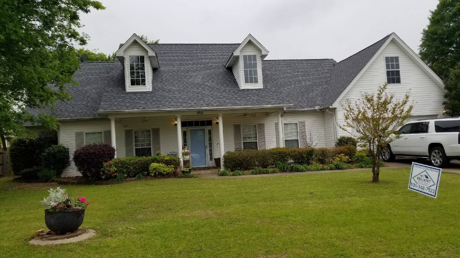 A white house with a gray roof and a blue door is sitting on top of a lush green lawn.