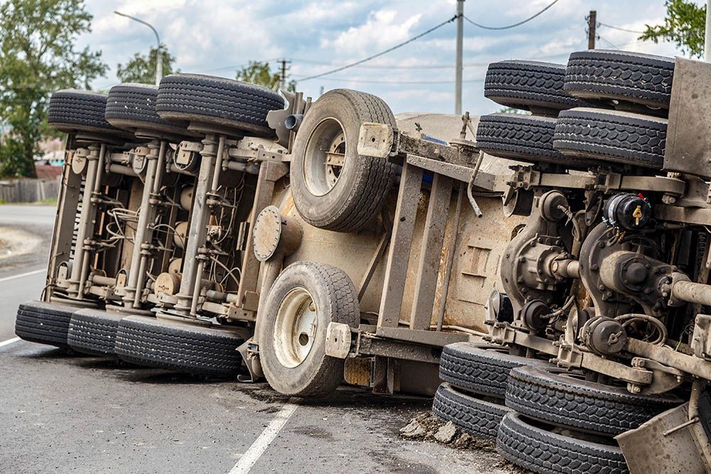 Overturned truck blocking road, wheels exposed and cargo spilled on the pavement