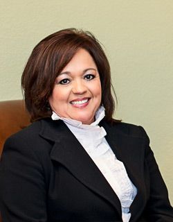 Smiling professional in a black blazer and white blouse seated against a beige background