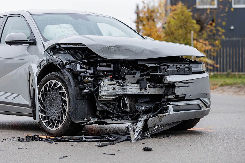 Damaged silver car with severe front-end crash damage on a street.