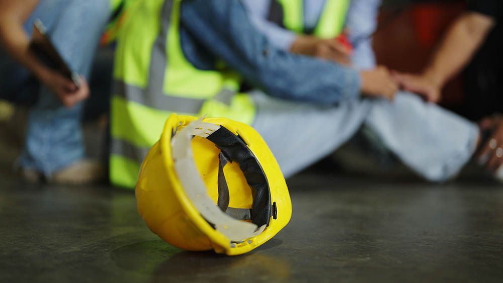 Yellow construction hard hat on the floor with workers in reflective vests sitting blurred in the background