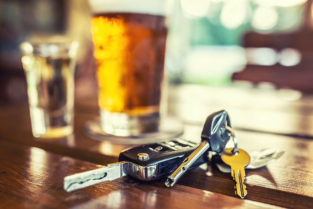 Car keys on a wooden table beside a glass of beer in a dimly lit bar