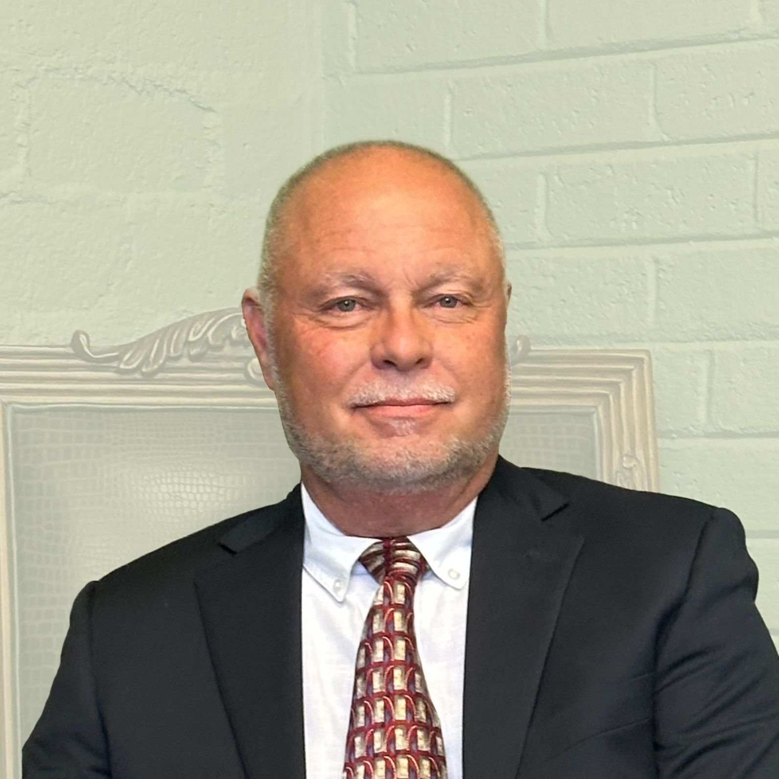 Man in a dark suit and patterned tie posing against a light brick wall