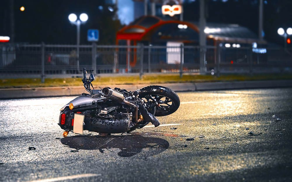 Overturned motorcycle on a wet road at night near a bus stop, with streetlights in the background