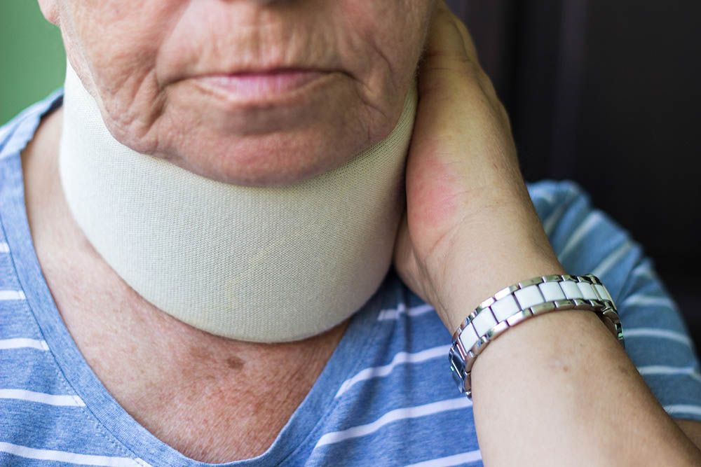 Person wearing a white neck brace holding the side of their neck, with a watch and blue striped shirt.