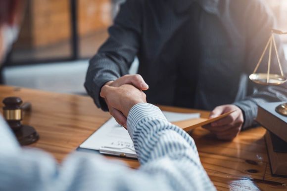 Two people shaking hands over a desk with documents and a gavel in a law office