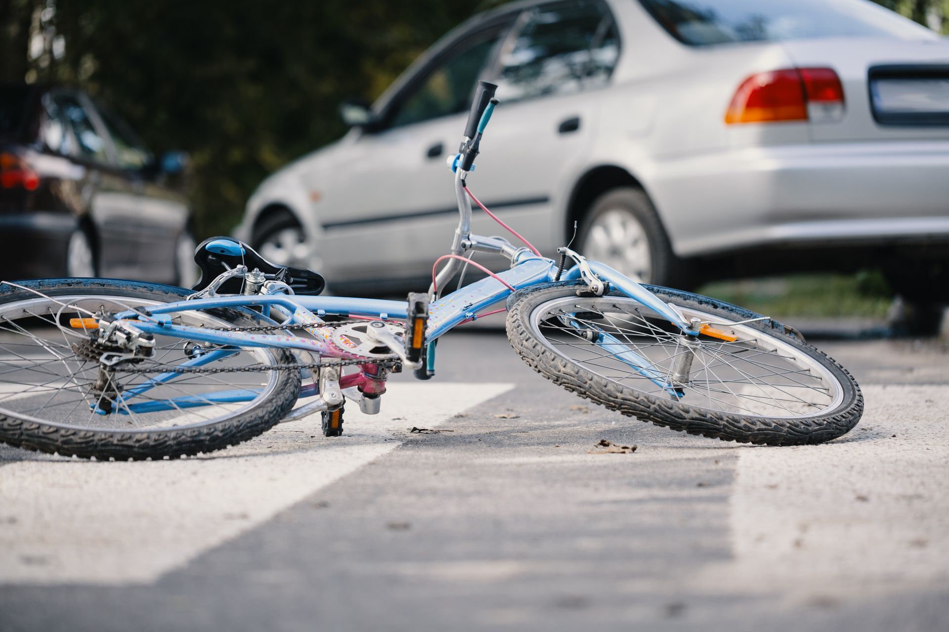Overturned blue bicycle lying on a street beside a parked silver car