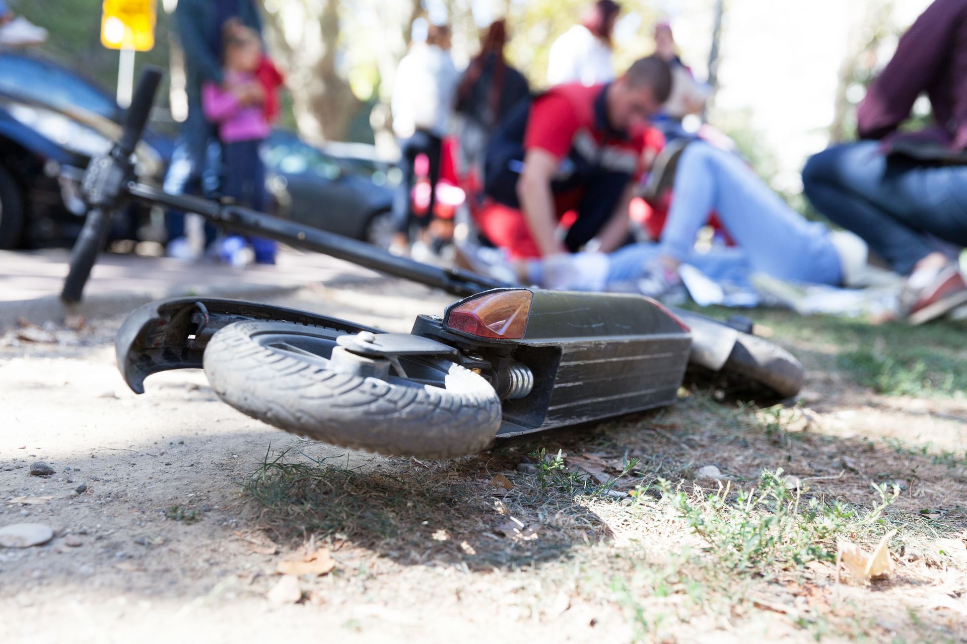 A bicycle lying on its side on a grassy path, with a blurred group of people in the background.