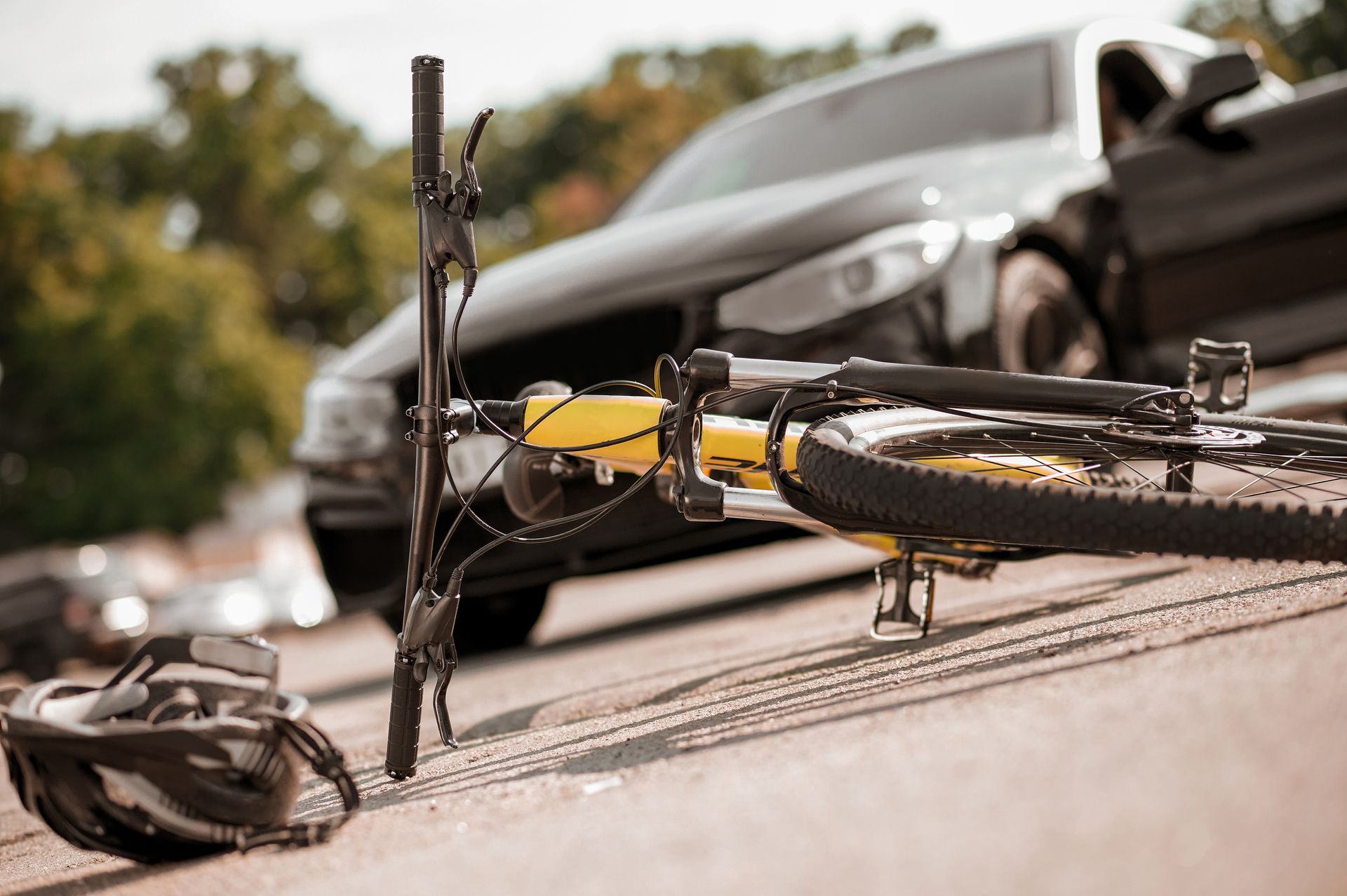 Broken bicycle in foreground after car crash on a road, with damaged car behind it
