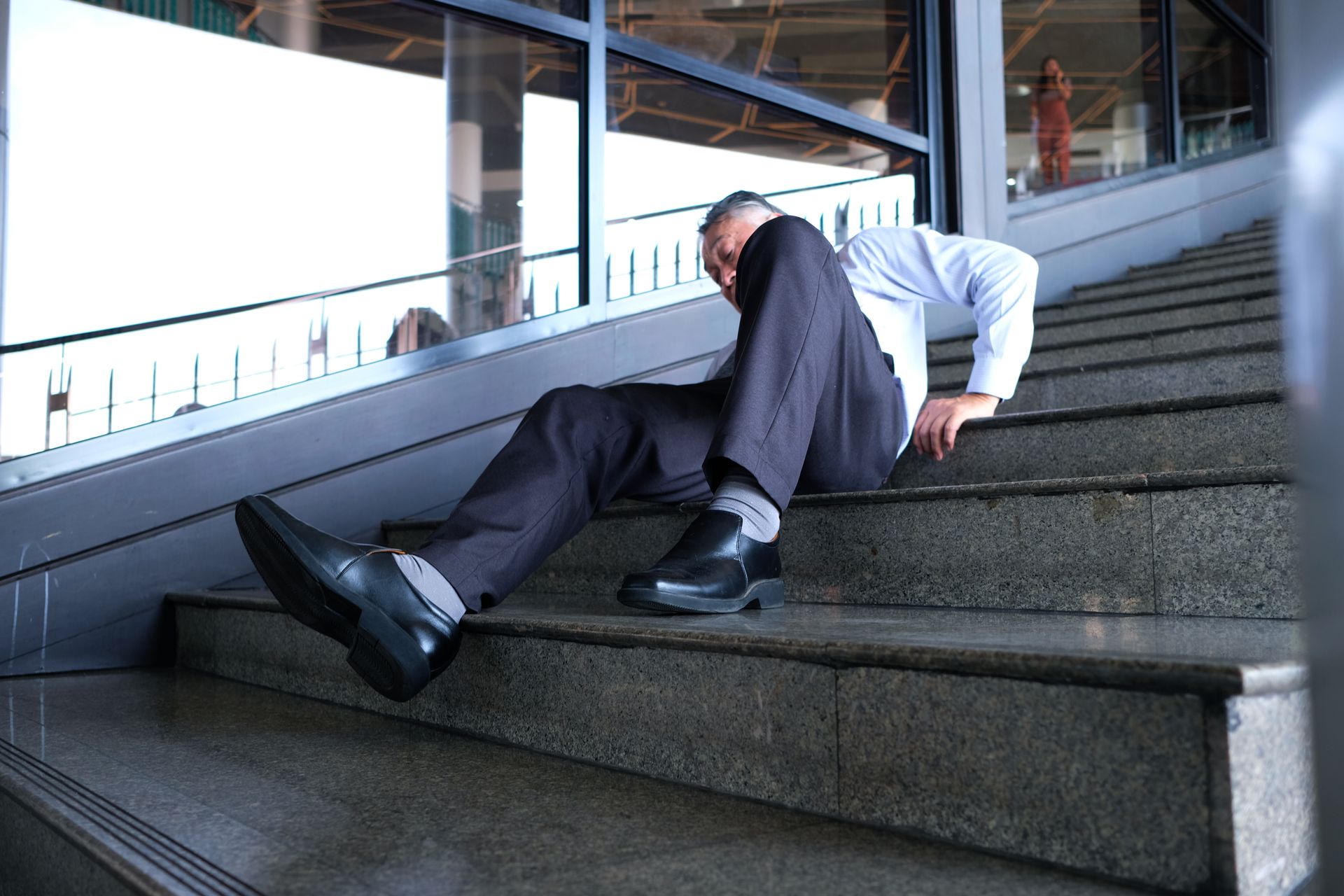 Man lying awkwardly on concrete stairs in a modern building interior