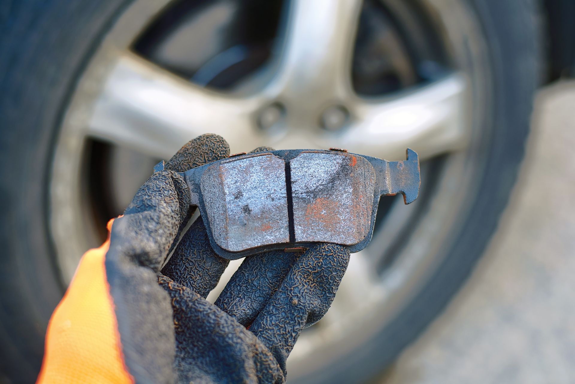 Gloved hand holding a worn brake pad in front of a car wheel