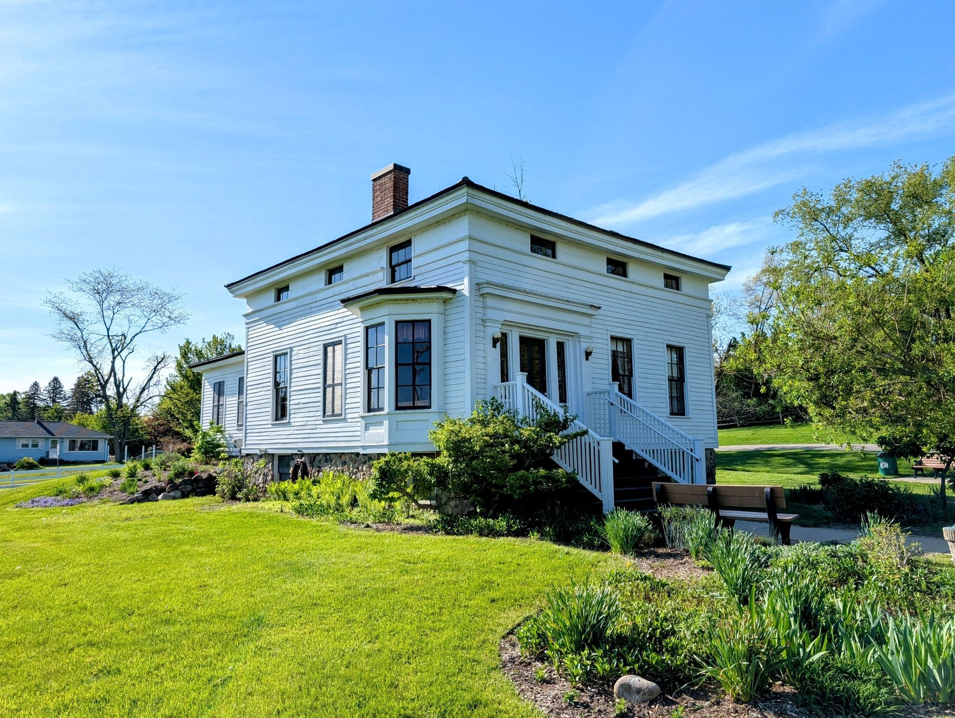 White farmhouse with porch and chimney in a sunny green yard under a blue sky