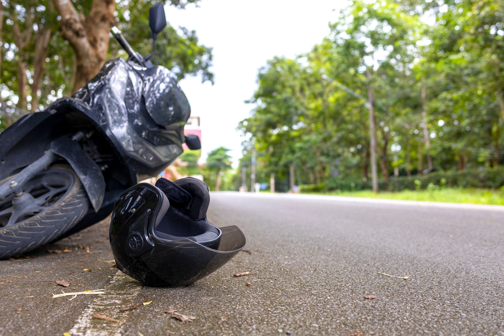 Severely damaged motorcycle lying on its side on a roadside under trees