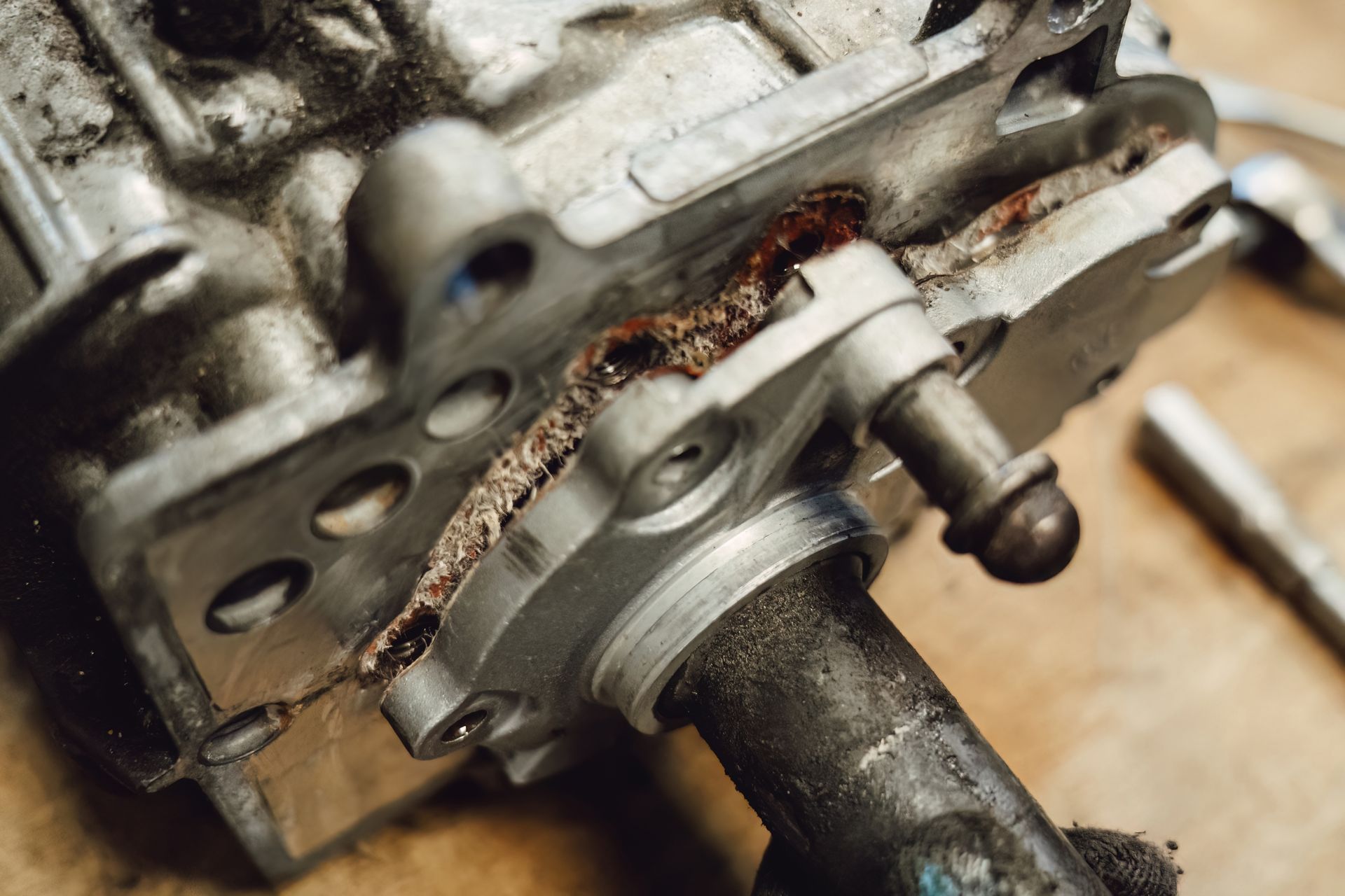 Close-up of a rusty metal engine part with a hose or shaft attached, resting on a workbench