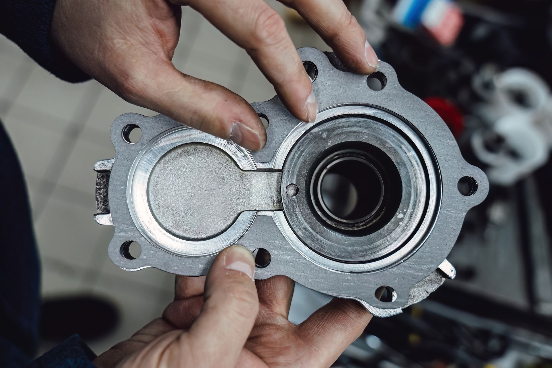 Hands holding a silver metal mechanical part with circular openings and bolts.