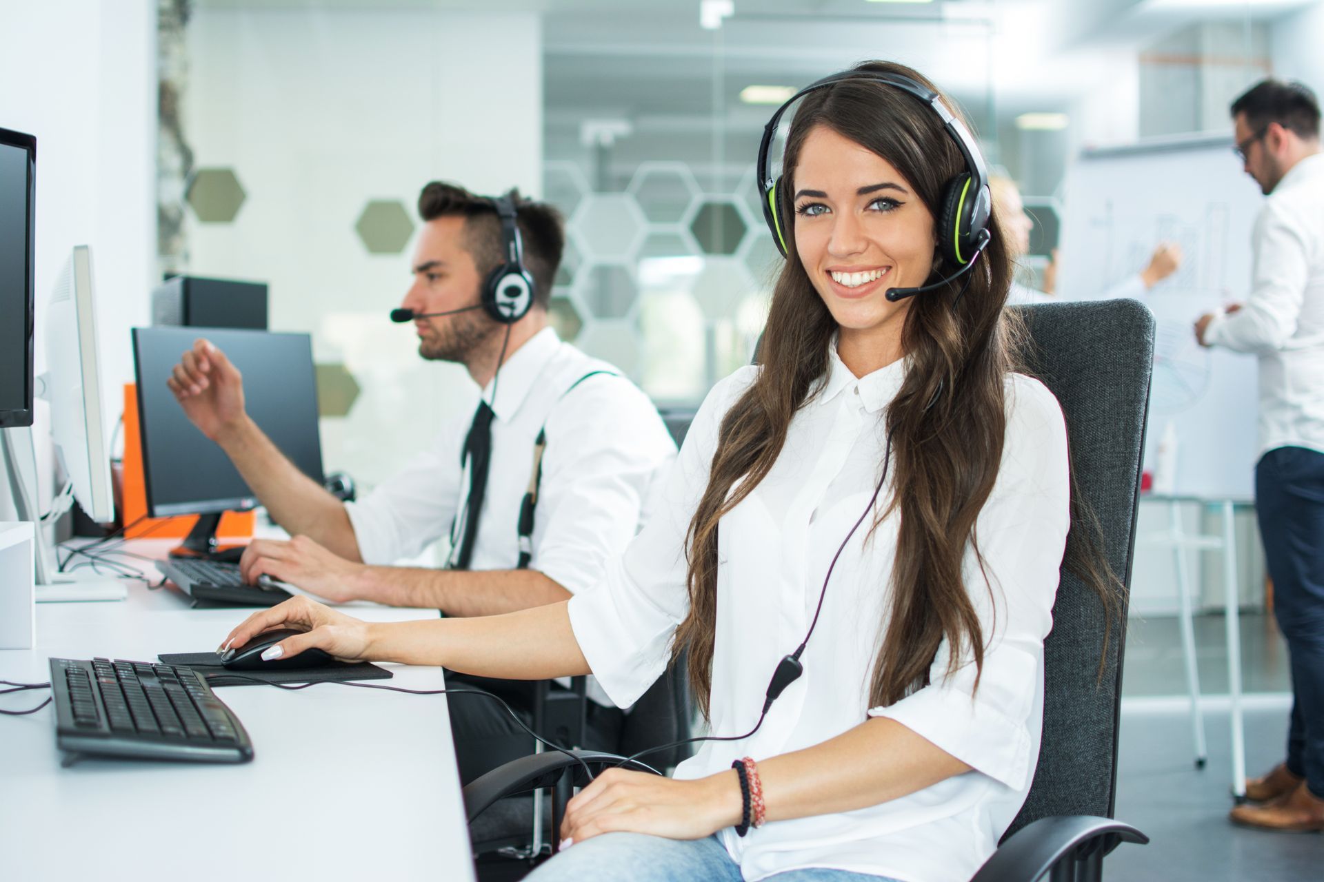 Call center agents wearing headsets at desks in a bright office, one smiling at the camera