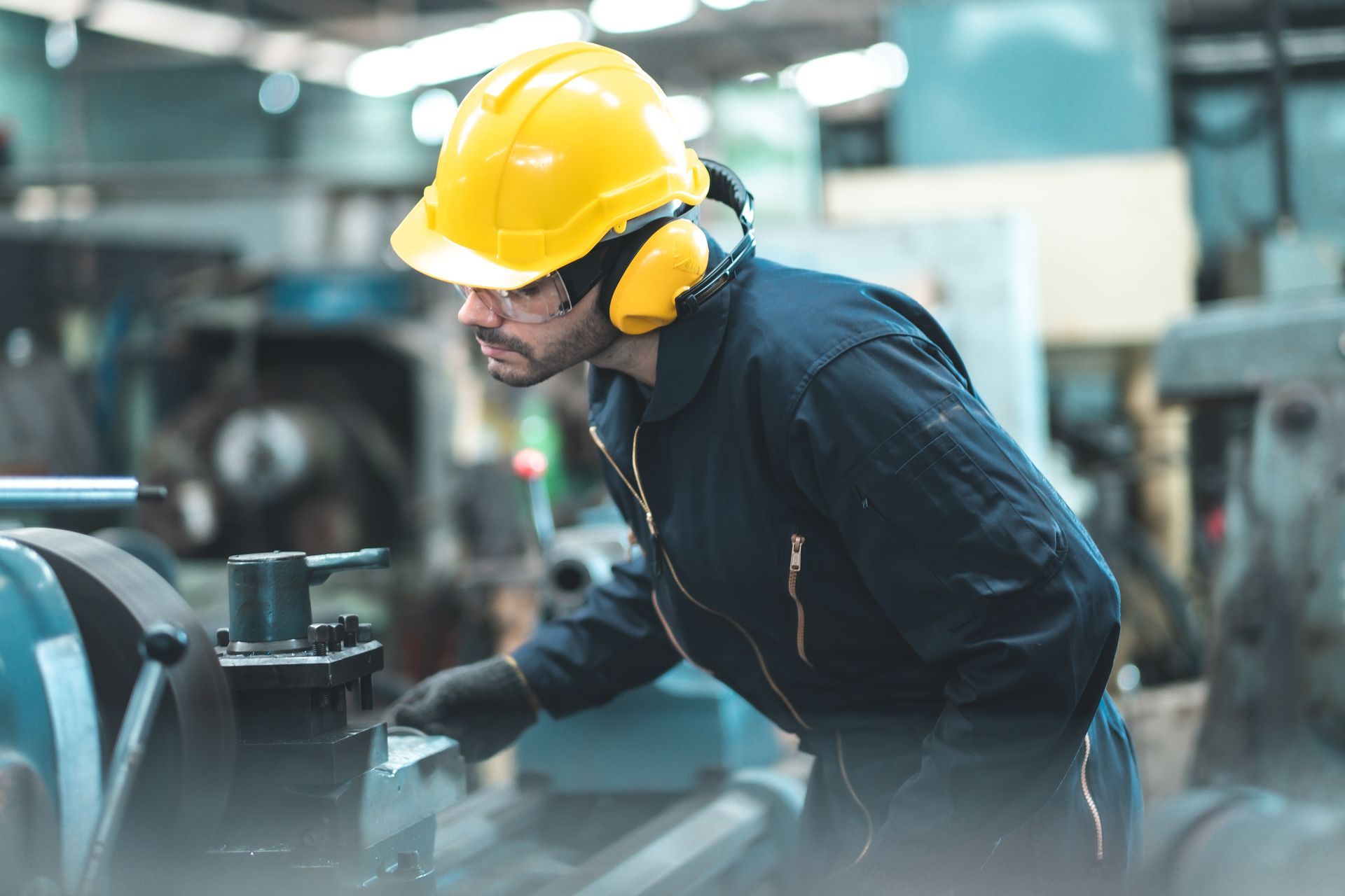 Warehouse worker in yellow hard hat reviewing paperwork at a computer in a stocked warehouse