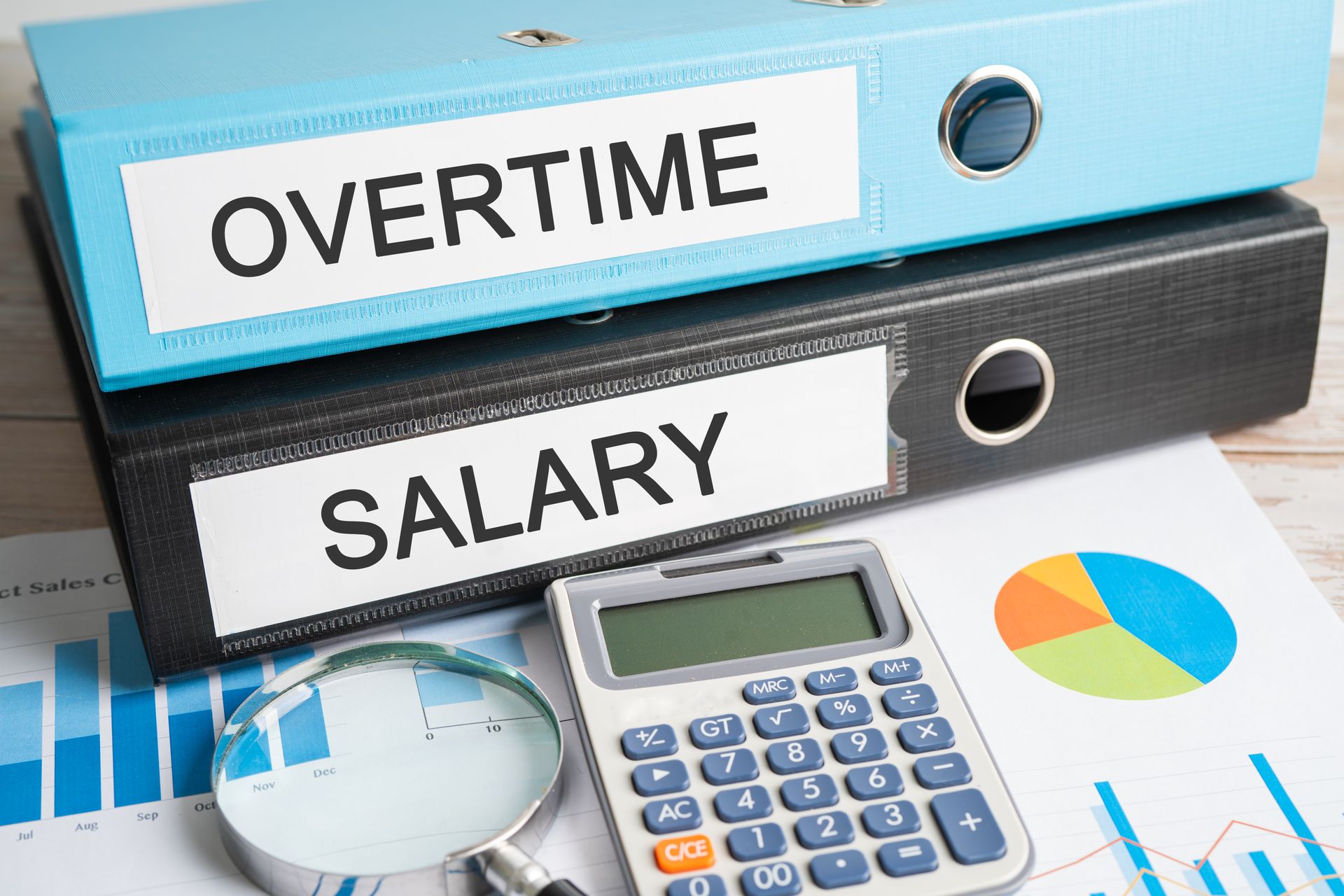 Overtime and salary folders with calculator, magnifying glass, and charts on a desk