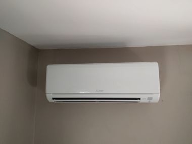 Wall-mounted white air conditioner on a gray wall near the ceiling