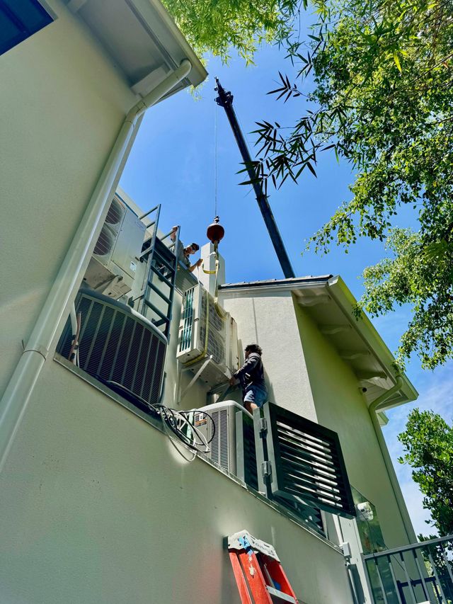 Three outdoor air conditioning units beside a white building and green shrubs