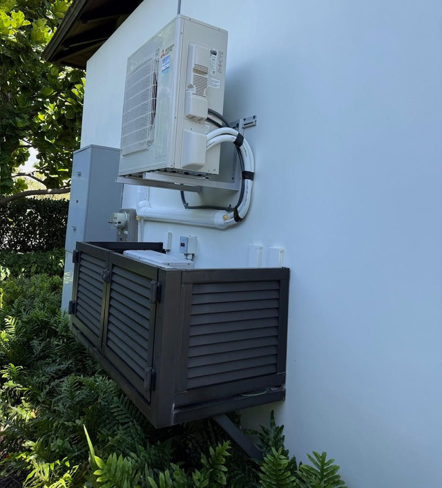Outdoor air-conditioning units mounted on a white exterior wall beside greenery