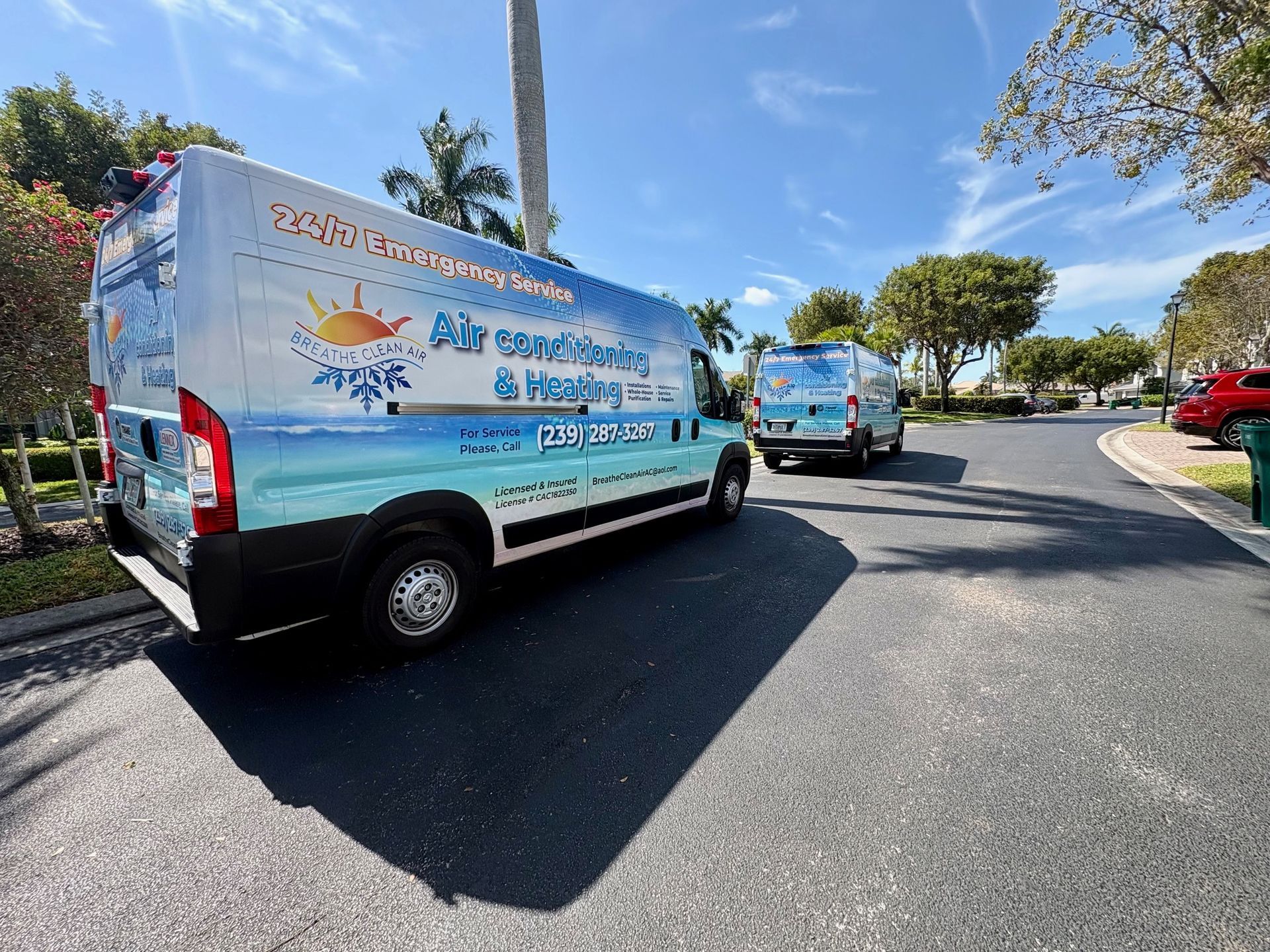 Two blue-and-white service vans parked on a sunny roadside, one in the foreground and one ahead.