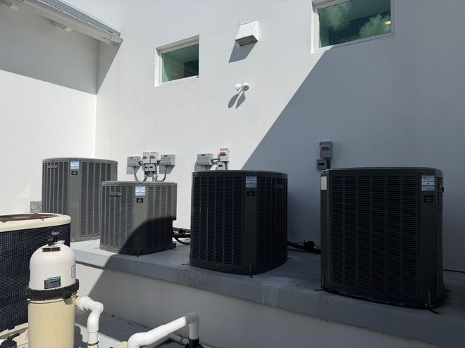 Four outdoor air conditioning units beside a white building in bright sunlight