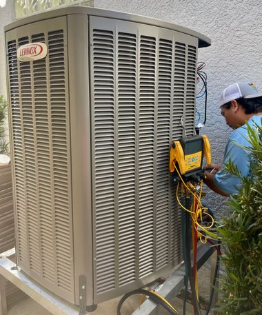 Technician inspecting a large beige outdoor air conditioner with a yellow meter in a courtyard