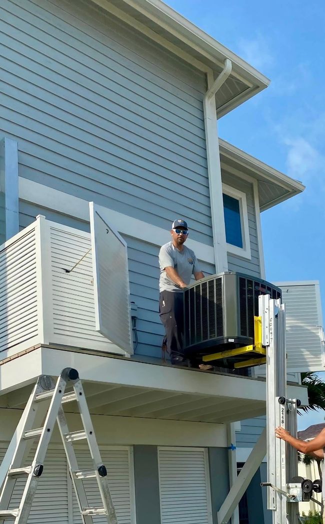 Worker on a balcony operating a yellow lift beside a blue house