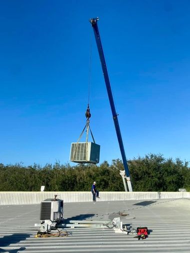 Crane lifting a large concrete block over a flat rooftop under a clear blue sky.