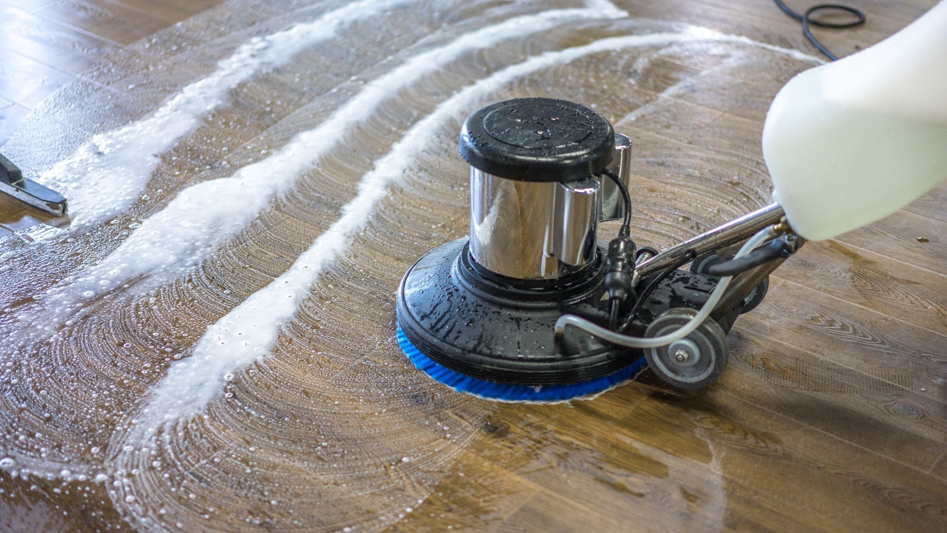A person is cleaning a wooden floor with a machine.