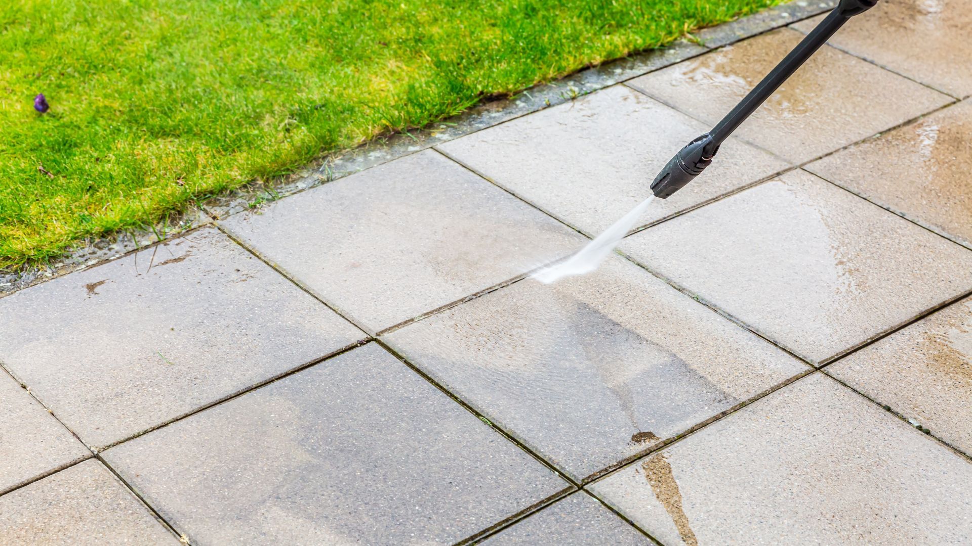 A person is using a high pressure washer to clean a patio.
