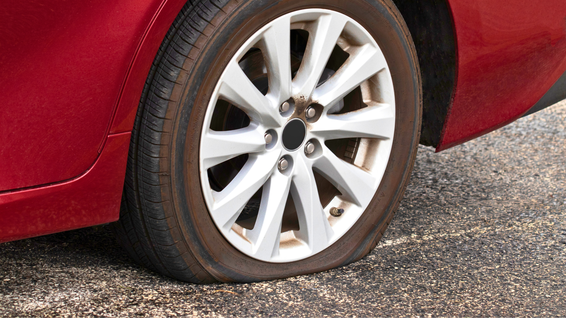 Person removing a car tire beside a silver vehicle with a jack on a driveway