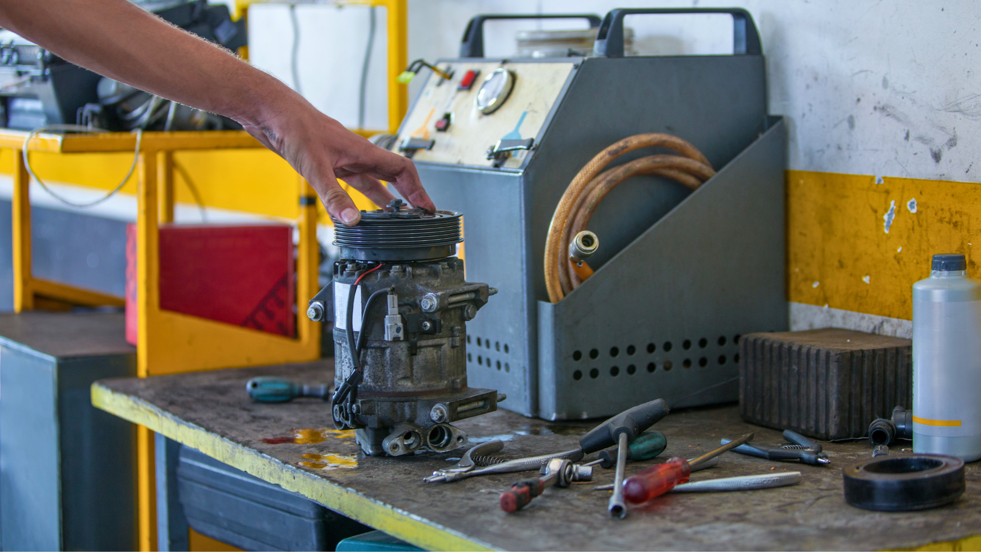 Hand repairing a metal machine on a workbench in a workshop, with tools and equipment nearby