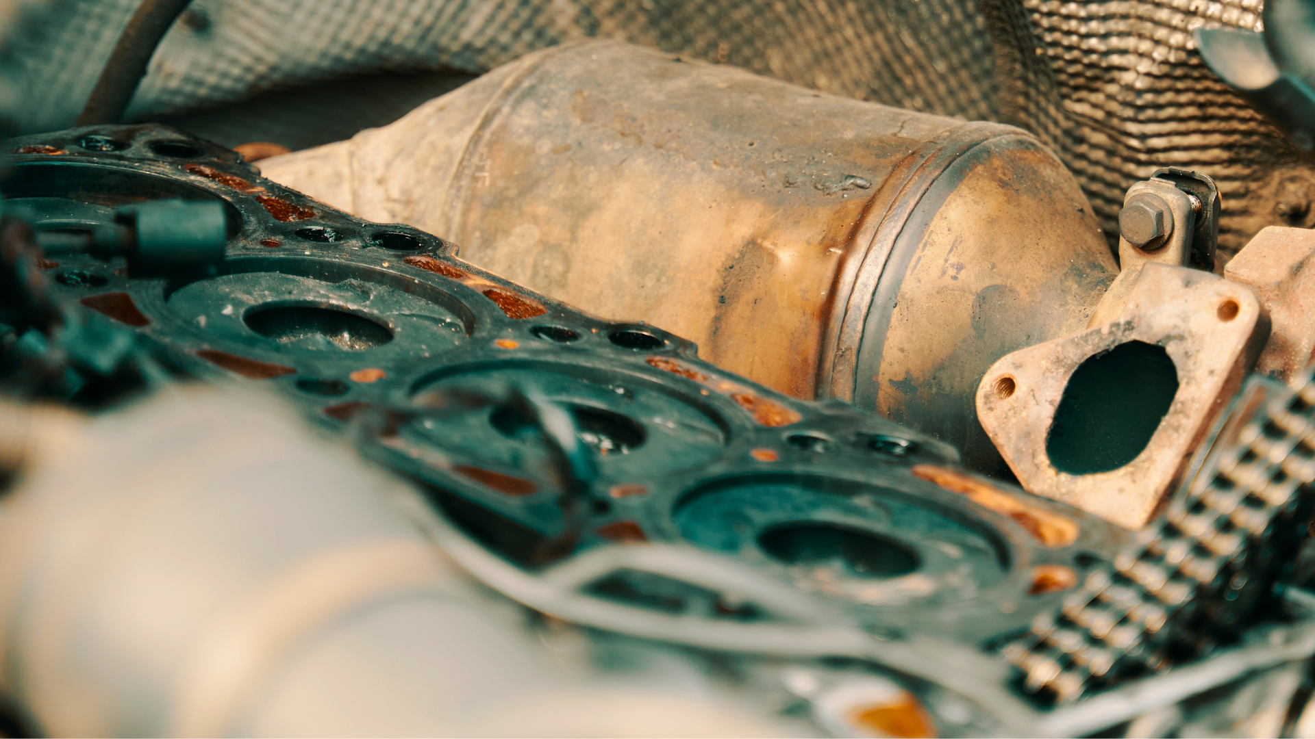 Pile of used car parts including a rusted exhaust pipe and metal gasket on a cloth surface