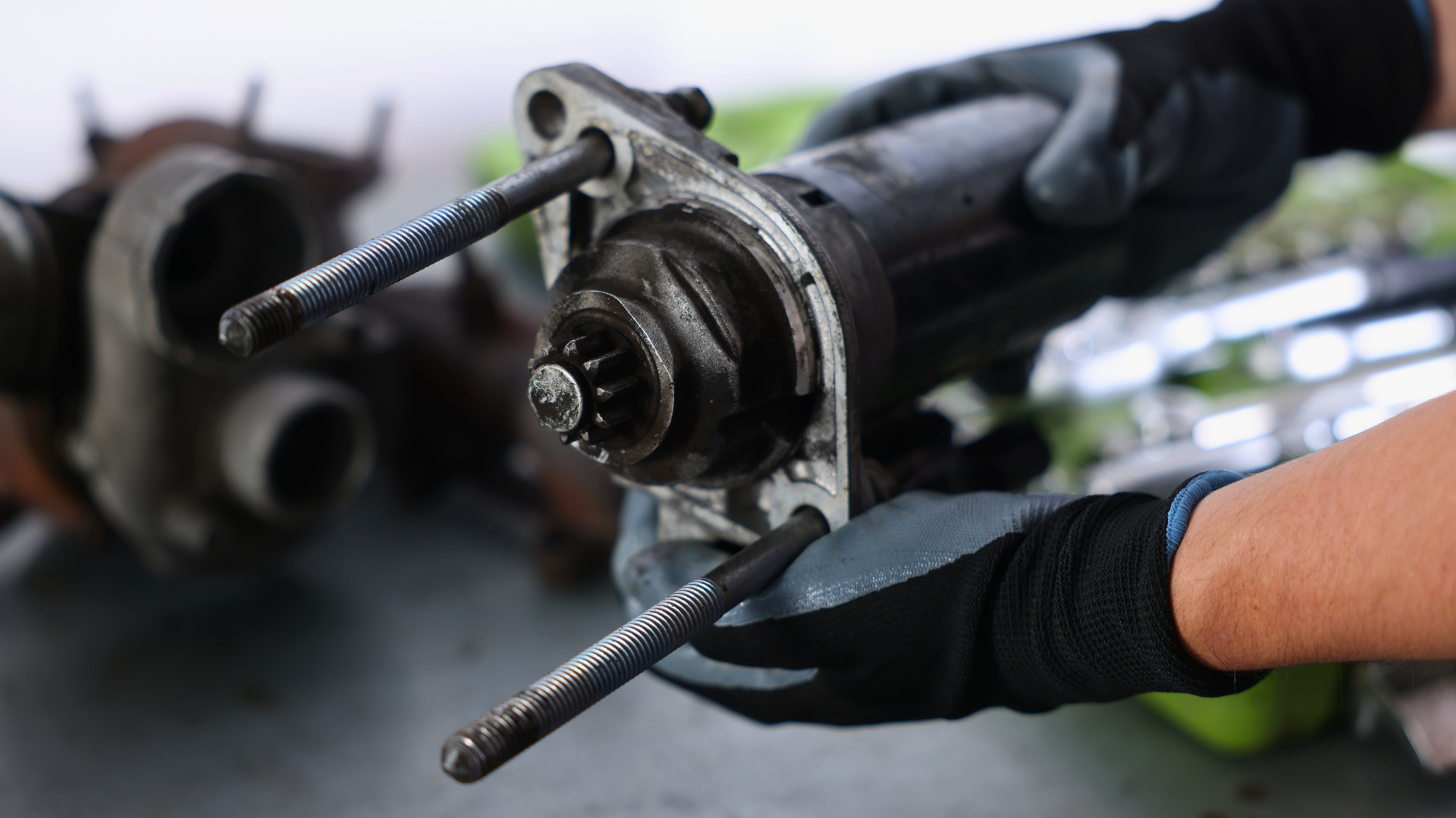 Gloved hands holding a used car axle with wheel hub and bolts, close-up in a workshop.
