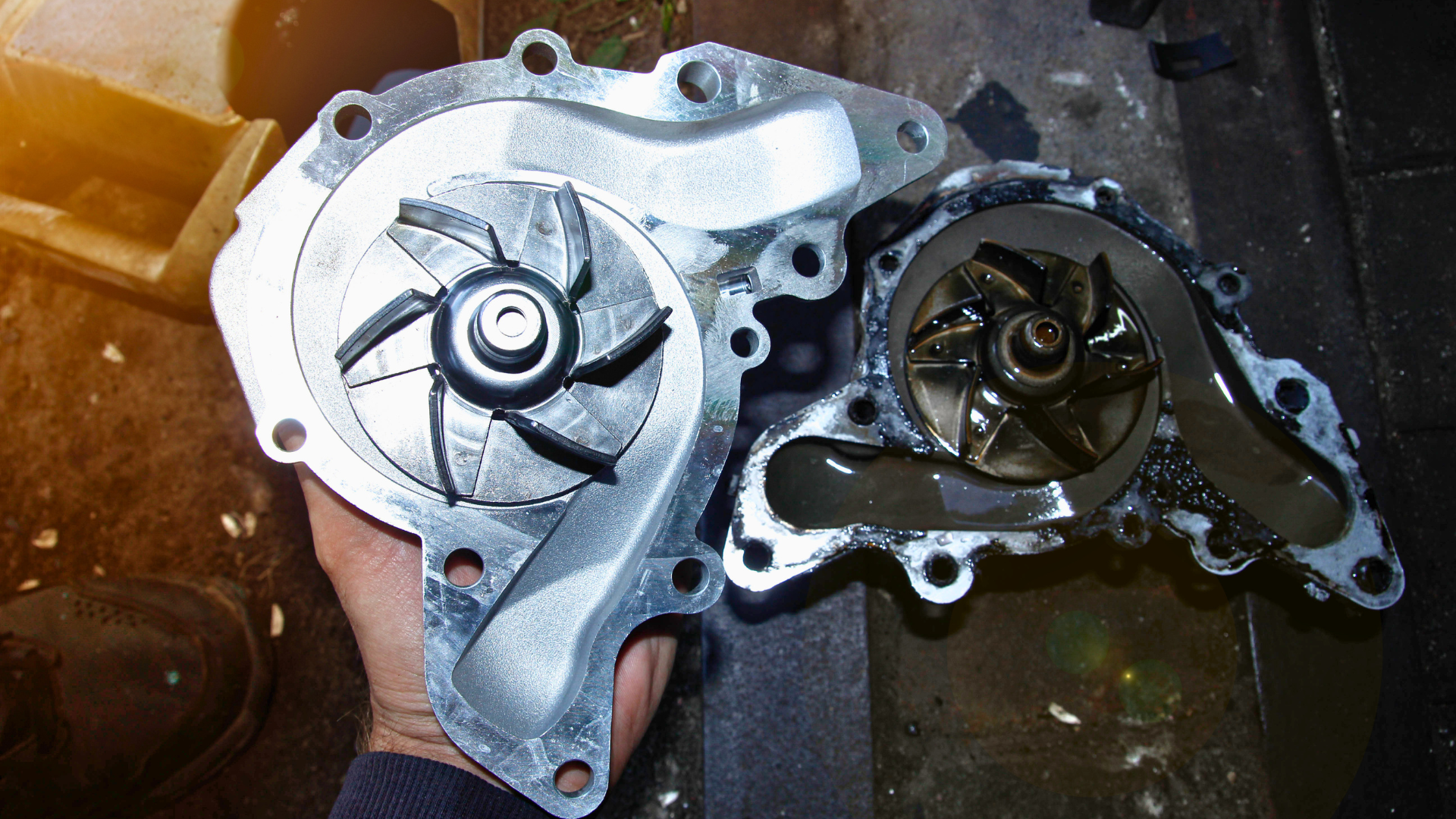 Two metal engine water pump housings side by side on a dark work surface.