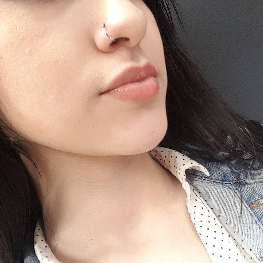 Woman with nose ring, wearing denim jacket, looking slightly down.