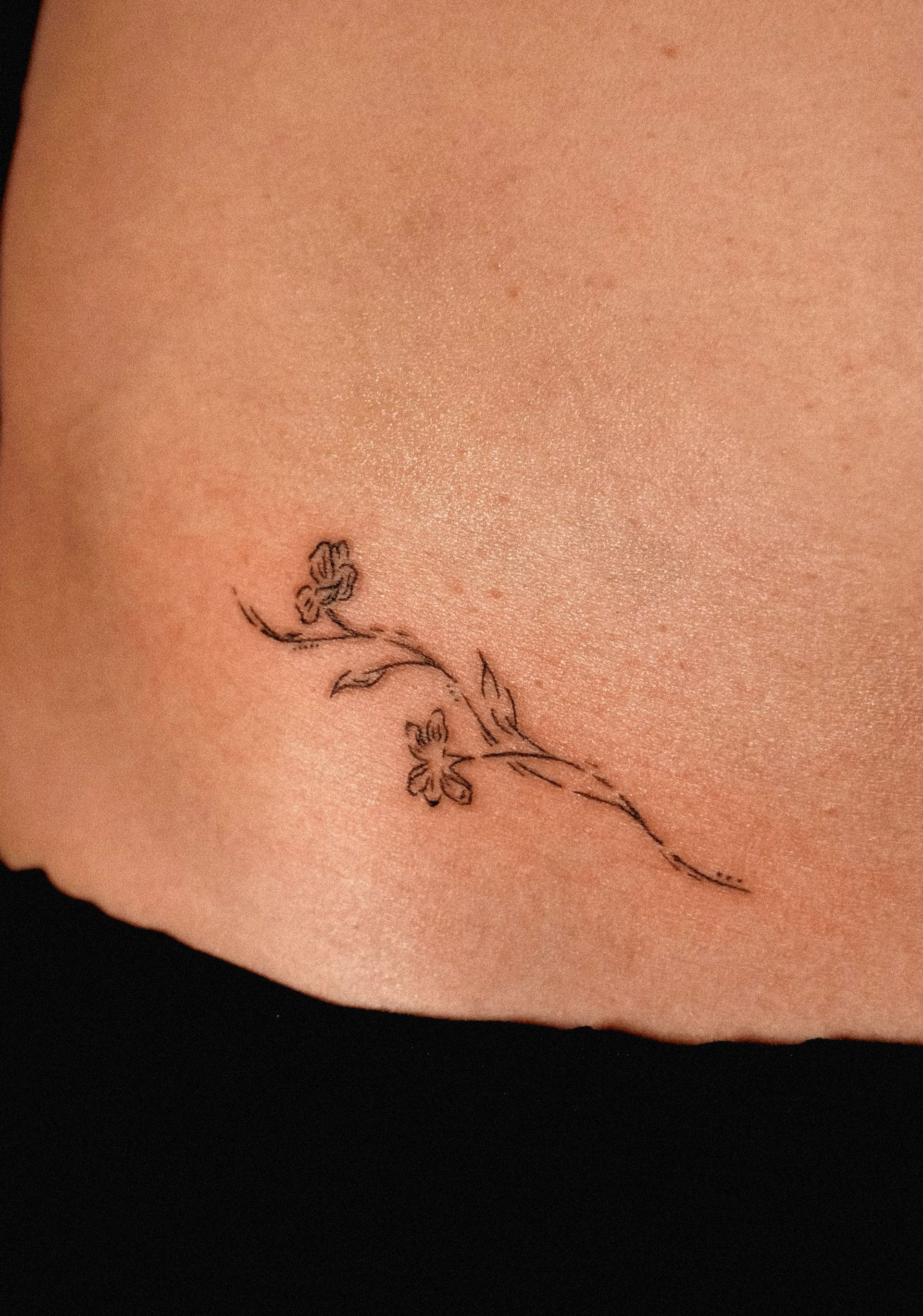 Delicate black flower tattoo on a person's skin, a slender branch with tiny blossoms.