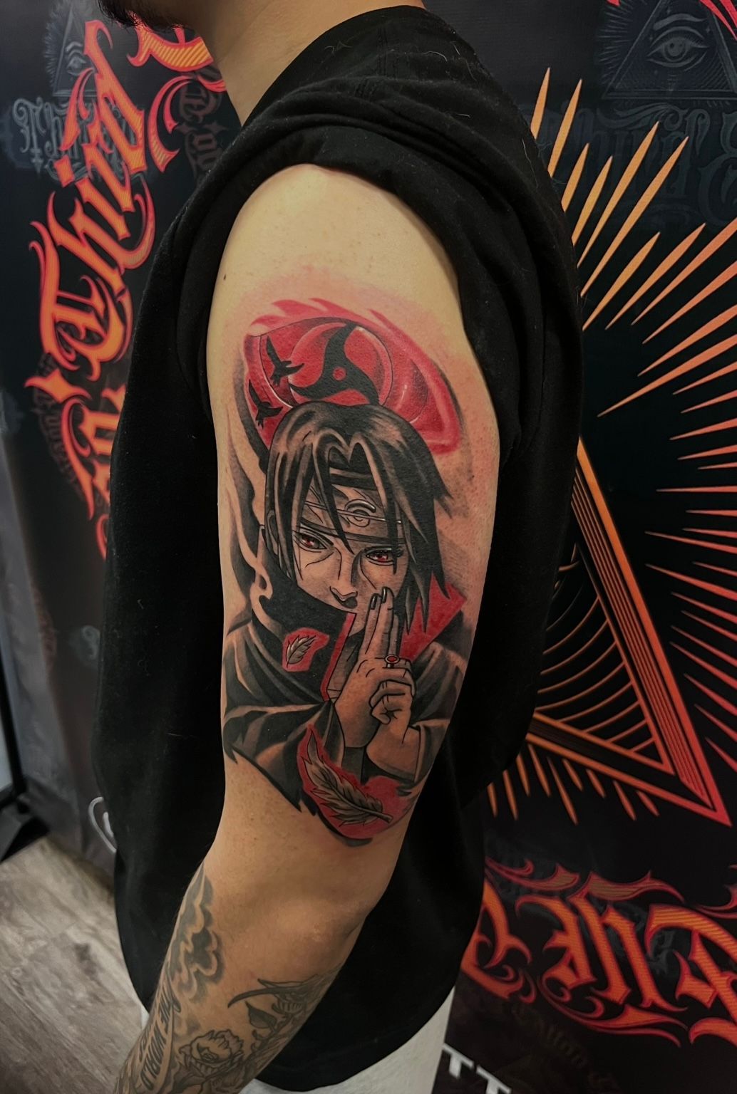 A person's arm with an Itachi Uchiha tattoo. Red and black ink with anime character doing a hand gesture.