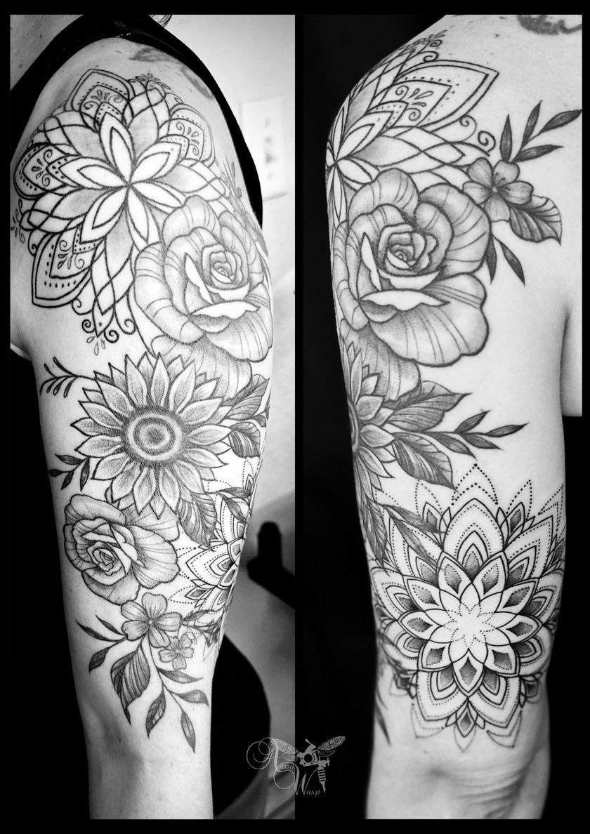 Black and white floral tattoo on a person's upper arm, featuring roses, sunflowers, and mandala designs.